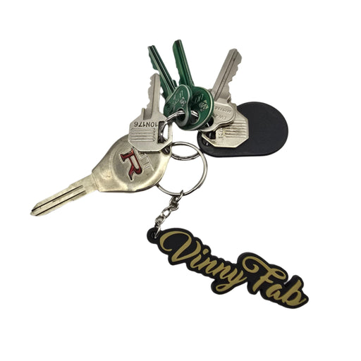 Vinny Fab keychain with gold cursive lettering on a black background, attached to a metal key ring and chain.