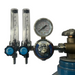 An oxygen regulator setup with two clear flow meters, a round analog pressure gauge, and blue adjustment knobs, attached to a blue gas cylinder against a plain white background.